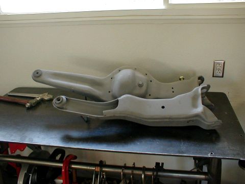 1996 Ford Bronco - Two suspension control arms and a differential housing are shown on a workbench, likely for a vehicle's front suspension system.