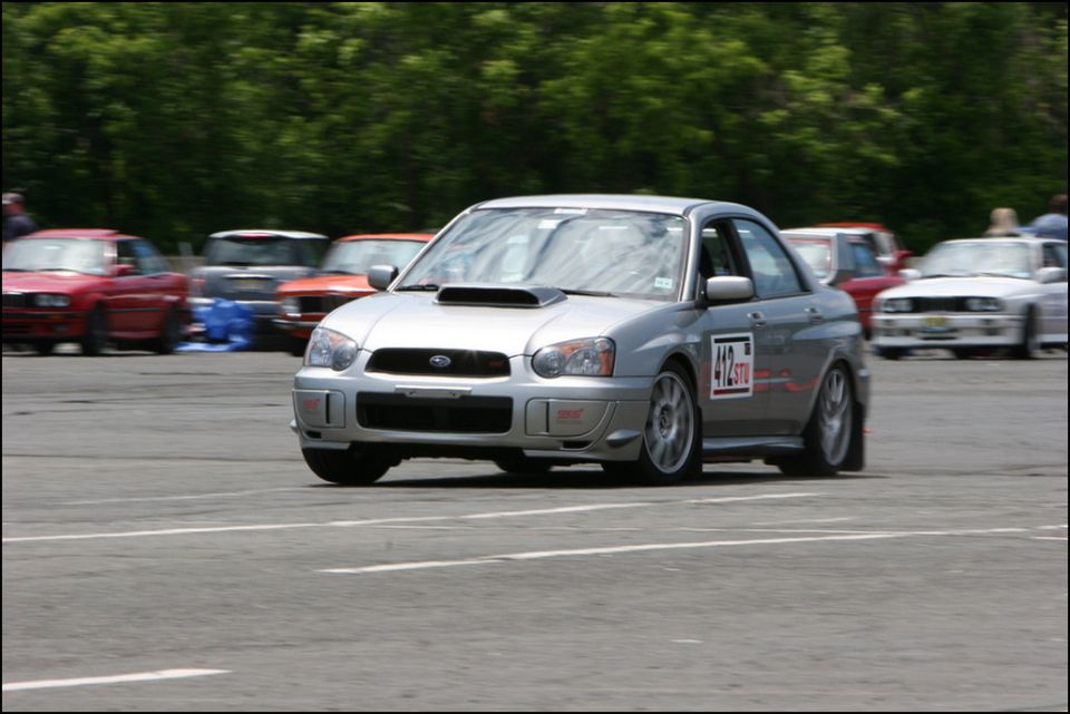 Silver Subaru Impreza WRX STI with racing number 412 STU on door, driving on asphalt track with other cars blurred in background