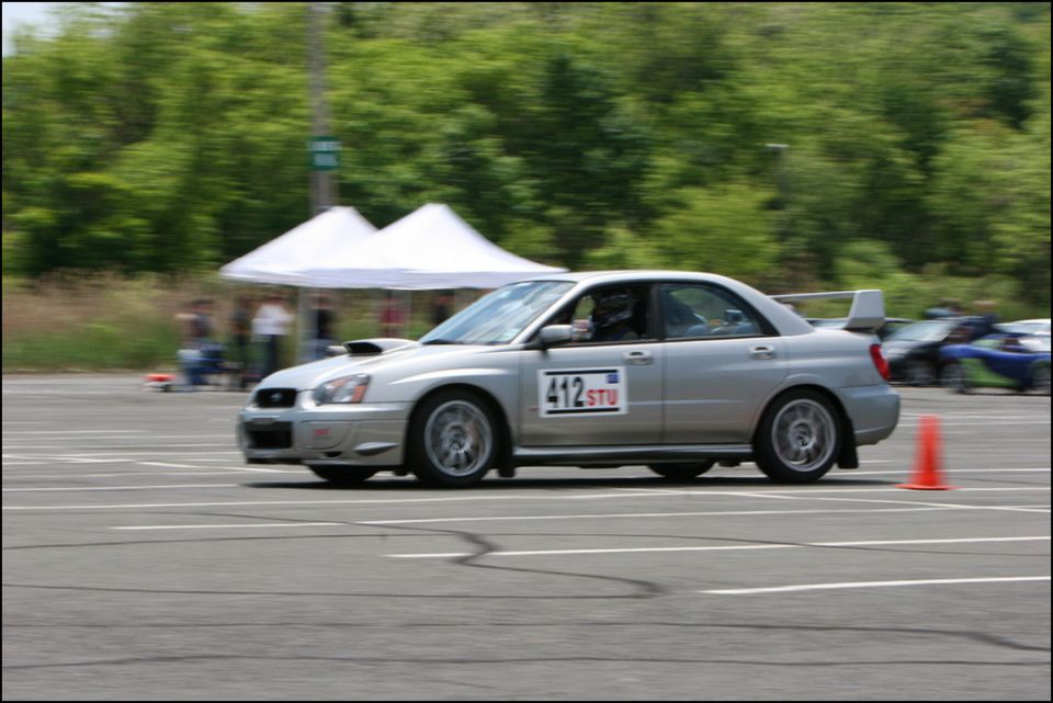 Silver Subaru Impreza WRX STI sedan with racing numbers on the door, driving on a track with orange cones
