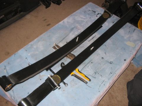 1991 Ford Bronco - Two black leaf springs, possibly for a vehicle modification, are laid out on a blue cloth with tools nearby. One spring has a brass tag wit…