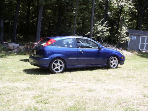2001 Mercury Grand Marquis - A blue hatchback is parked on a grassy lawn next to a wooded area and a small shed.