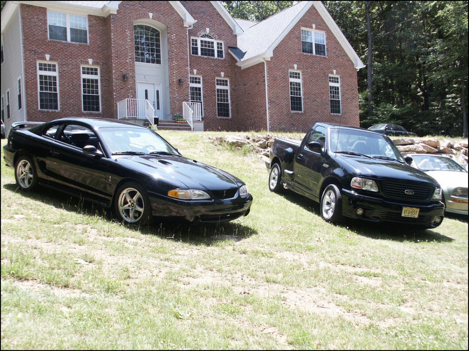 Black Ford Mustang and Ford F-150 pickup truck parked on lawn in front of brick house