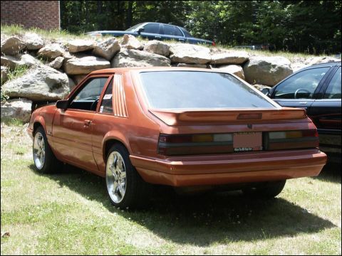 2001 Mercury Grand Marquis - Rear view of an orange coupe with louvers and aftermarket wheels, parked outdoors.