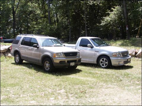 2001 Mercury Grand Marquis - Two trucks, a Ford Explorer and a Ford F-150 Lightning, are parked on a lawn in front of a wooded area.