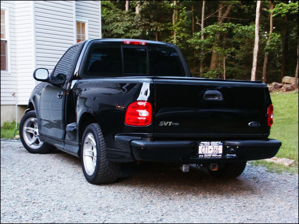 Black Ford SVT F-150 Lightning pickup truck, rear 3/4 view, parked on gravel