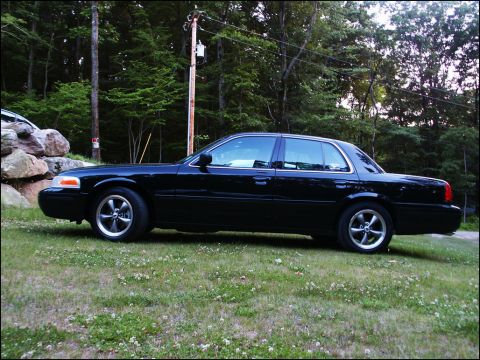2001 Mercury Grand Marquis - A black sedan is parked on a grassy area with trees and a utility pole behind it.
