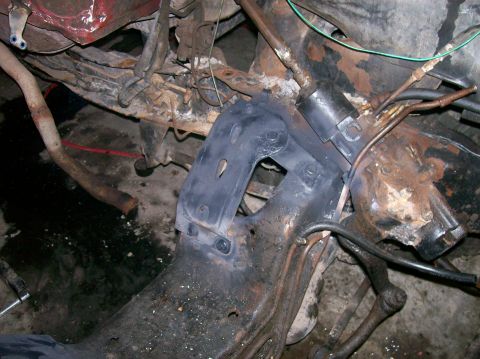 1982 Ford Bronco - The underside of a vehicle shows heavily rusted frame components and suspension parts, with some wiring and exhaust pipe visible.