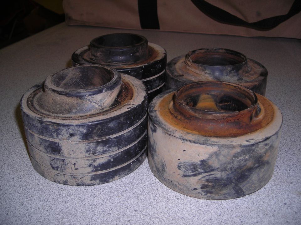 Four dirty black and rusty suspension lift spacers stacked on a speckled surface