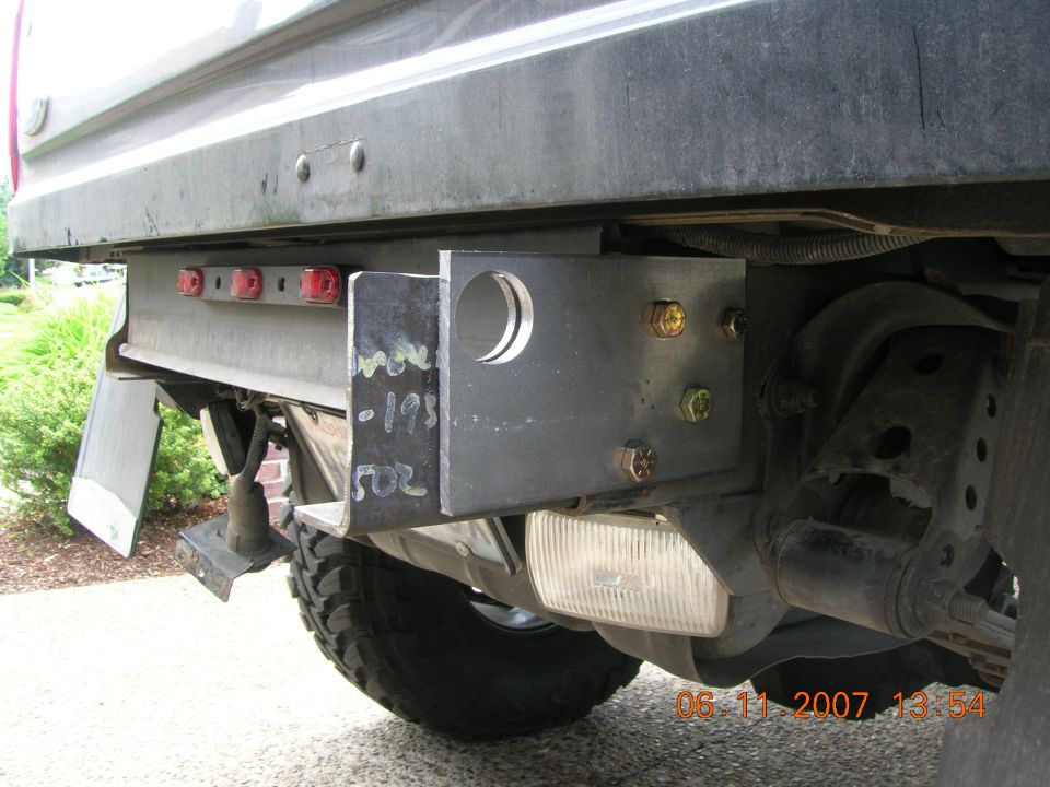 Bare steel custom receiver hitch bolted under rear bed of lifted truck