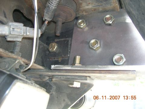 1996 Ford Bronco - Close-up view of a vehicle's undercarriage, focusing on a bolted metal plate and suspension parts.