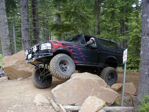 1994 Ford Explorer - A modified 1994 Ford Bronco navigates a challenging rocky trail with flame decals adorning its sides.
