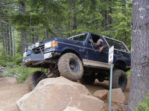 1994 Ford Explorer - A modified Ford Bronco navigates a rocky off-road course in a wooded area.