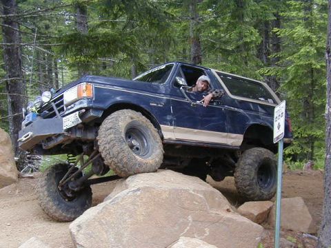 1994 Ford Explorer - A man drives a lifted Ford Bronco over large rocks on a trail.