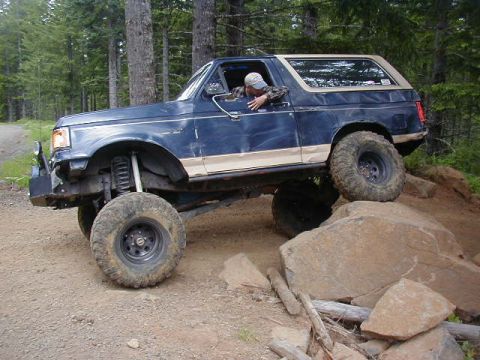 1994 Ford Explorer - Modified Ford Bronco tackling a challenging off-road course with large rocks and trees.
