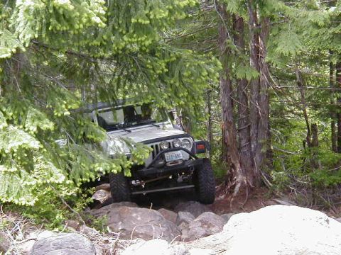 1994 Ford Explorer - A white Jeep Wrangler is seen off-roading through a rocky, wooded area.