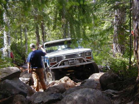 1994 Ford Explorer - Ford Bronco tackling a difficult rocky trail in a wooded area.