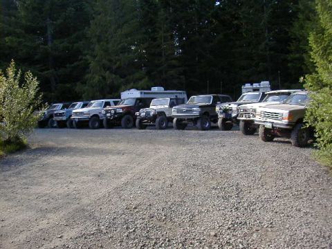 1994 Ford Explorer - Multiple SUVs and trucks are parked in a gravel lot with a wooded area behind them.