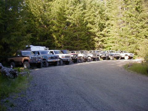 1994 Ford Explorer - Multiple SUVs and trucks are parked on a gravel road beside a dense forest.