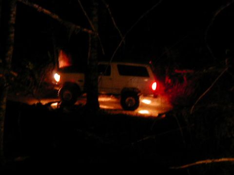 1994 Ford Explorer - A white SUV is seen from the side at night, with its headlights and taillights on, partially obscured by trees.