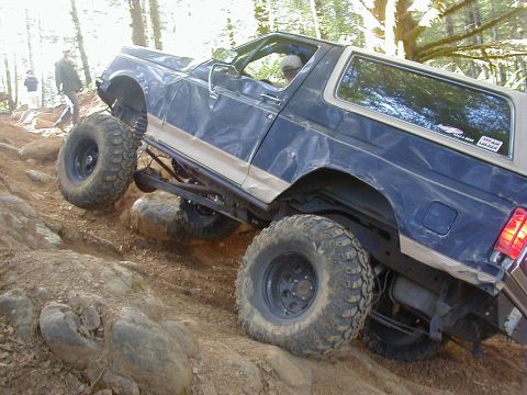 1994 Ford Explorer - A modified Ford Bronco navigates a challenging rocky incline in a wooded area.