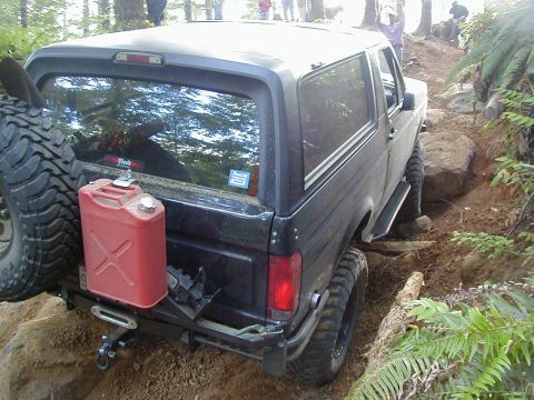 1994 Ford Explorer - A black Ford Bronco navigates a challenging off-road trail with large rocks and dense foliage.