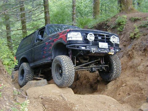 1994 Ford Explorer - Modified black Ford Bronco with flame decals navigates a rocky trail.