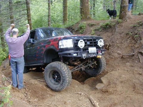 1994 Ford Explorer - Off-road Bronco II navigating a steep, rocky incline with a person cheering.