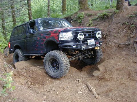1994 Ford Explorer - This modified Ford Bronco is navigating a challenging off-road trail with steep inclines and rocks.