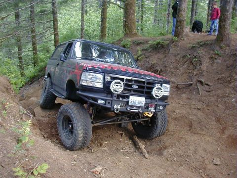 1994 Ford Explorer - Modified Ford Bronco navigates a steep, muddy incline in a wooded area.