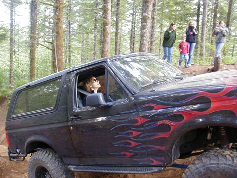 1994 Ford Explorer - A black SUV with flame decals and a "BRONCO" badge is shown off-road with people watching in the background.