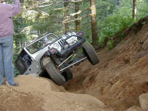 1994 Ford Explorer - A white Jeep Wrangler TJ navigates a challenging off-road trail, with one side significantly higher than the other.