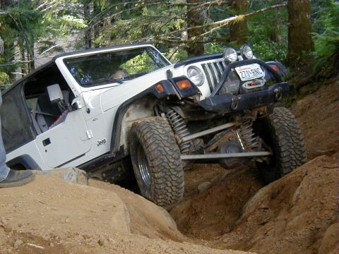 1994 Ford Explorer - A white Jeep Wrangler TJ navigates a challenging off-road obstacle on a wooded trail.