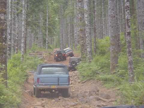 1994 Ford Explorer - Multiple SUVs traverse a challenging, rocky path through a dense forest.