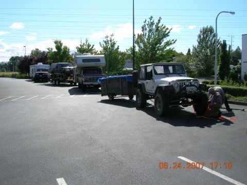 1996 Ford Bronco - A group of vehicles, including a Jeep and a pickup truck with a camper, are parked in a lot on a sunny day.