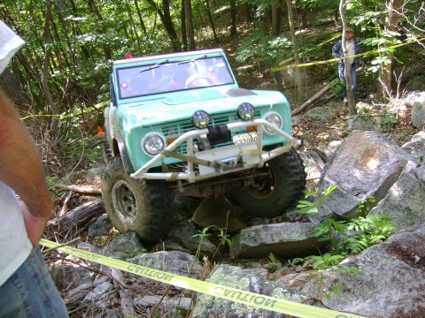 1969 Ford Bronco - A teal 1969 Ford Bronco navigates a rocky trail, equipped with a winch and auxiliary lights.