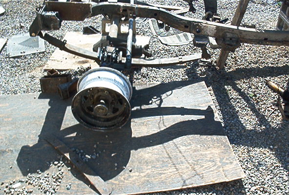 Vehicle frame assembly with a wheel resting on plywood, outdoors