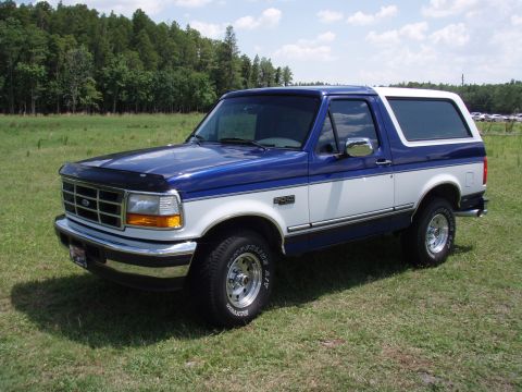 1996 Ford Bronco - This two-tone blue and white 1996 Ford Bronco is shown in a grassy field under a partly cloudy sky.