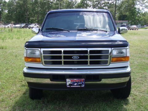 1996 Ford Bronco - This 1996 Ford Bronco is shown from the front, parked on a grassy area with trees in the background.
