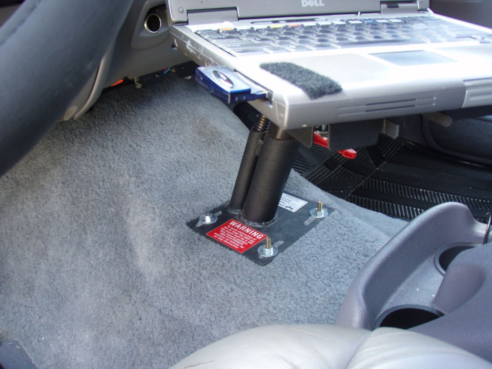 Laptop mount bolted to vehicle floor with warning label
