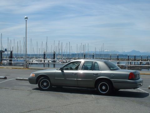 2000 Ford Crown Victoria - A 2000 Ford Crown Victoria sedan is parked near a marina with sailboats in the background.