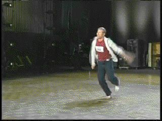 1991 Ford Bronco - A man wearing a red shirt, white jacket, and dark pants runs across a stage, with a bib number visible on his chest.