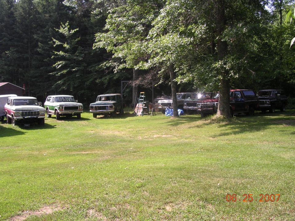 Several Ford trucks and SUVs parked in a yard, including a 1978 Ford Bronco. One vehicle has a 'For Sale' sign