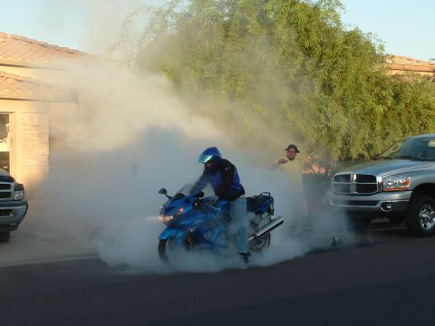 2007 Kawasaki Ninja - A motorcycle rider performs a burnout, creating a large cloud of smoke as a bystander and a pickup truck observe.