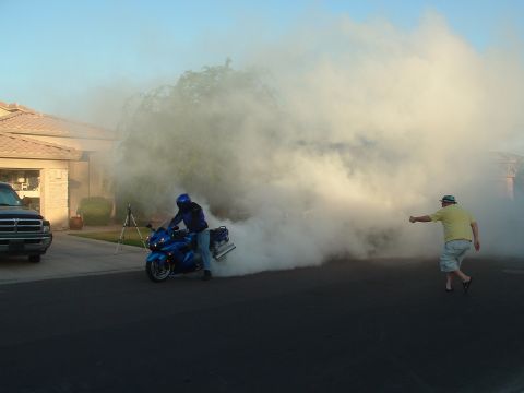 2007 Kawasaki Ninja - A motorcycle creates a large cloud of smoke while a person watches from the side of the road.