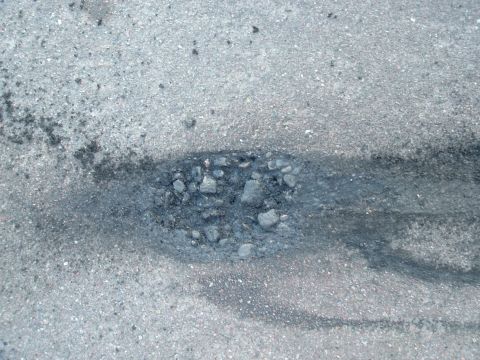 2007 Kawasaki Ninja - A pothole on an asphalt road shows damage and loose aggregate material.