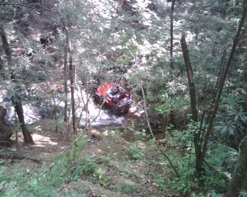 1987 Toyota 4Runner - A red off-road vehicle has crashed into a ditch surrounded by trees and foliage.