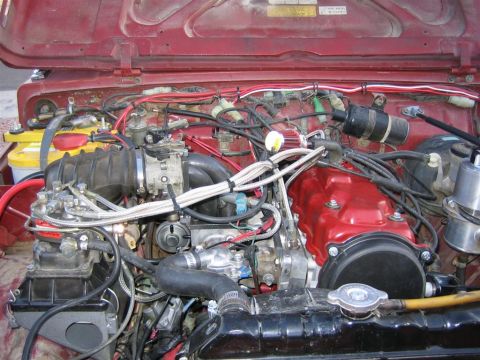 1987 Suzuki Samurai - Engine bay of a 1987 Suzuki Samurai, a red valve cover and a fuel injection system.