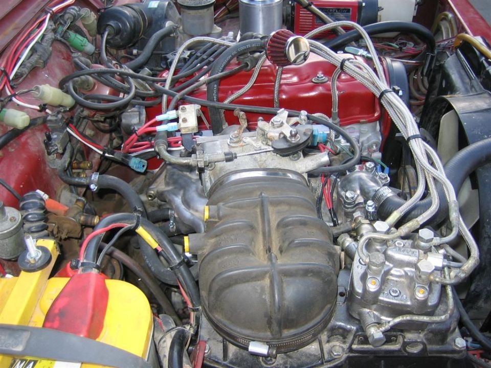 Engine bay from above with red valve cover, cast intake plenum, cone filter and A/C compressor