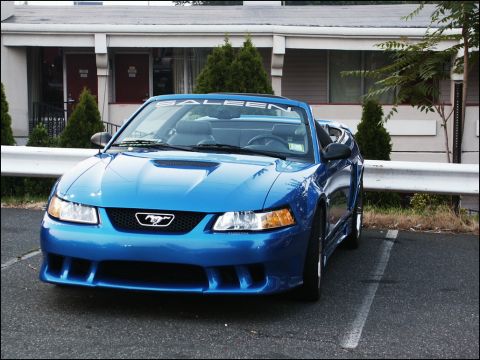 2001 Mercury Grand Marquis - A blue convertible sports car with a prominent 'SALEEN' banner on the windshield is parked in front of a motel-like building.