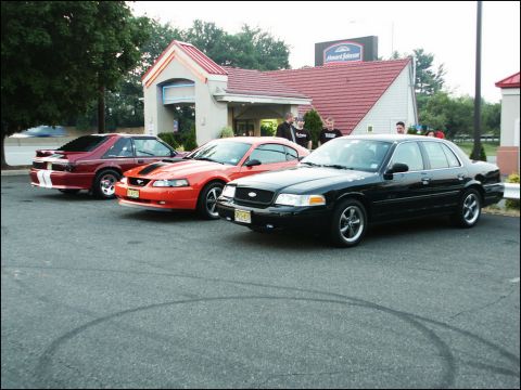 2001 Mercury Grand Marquis - Three cars, including two Ford Mustangs and a Crown Victoria, are parked in a lot in front of a hotel.